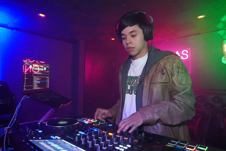 DJ Kev focused at the mixer under pink and green stage lighting