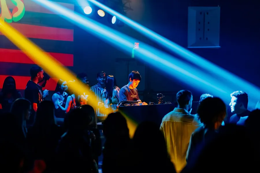 DJ Kev mixing on CDJs as blue and yellow light beams cut through the crowd